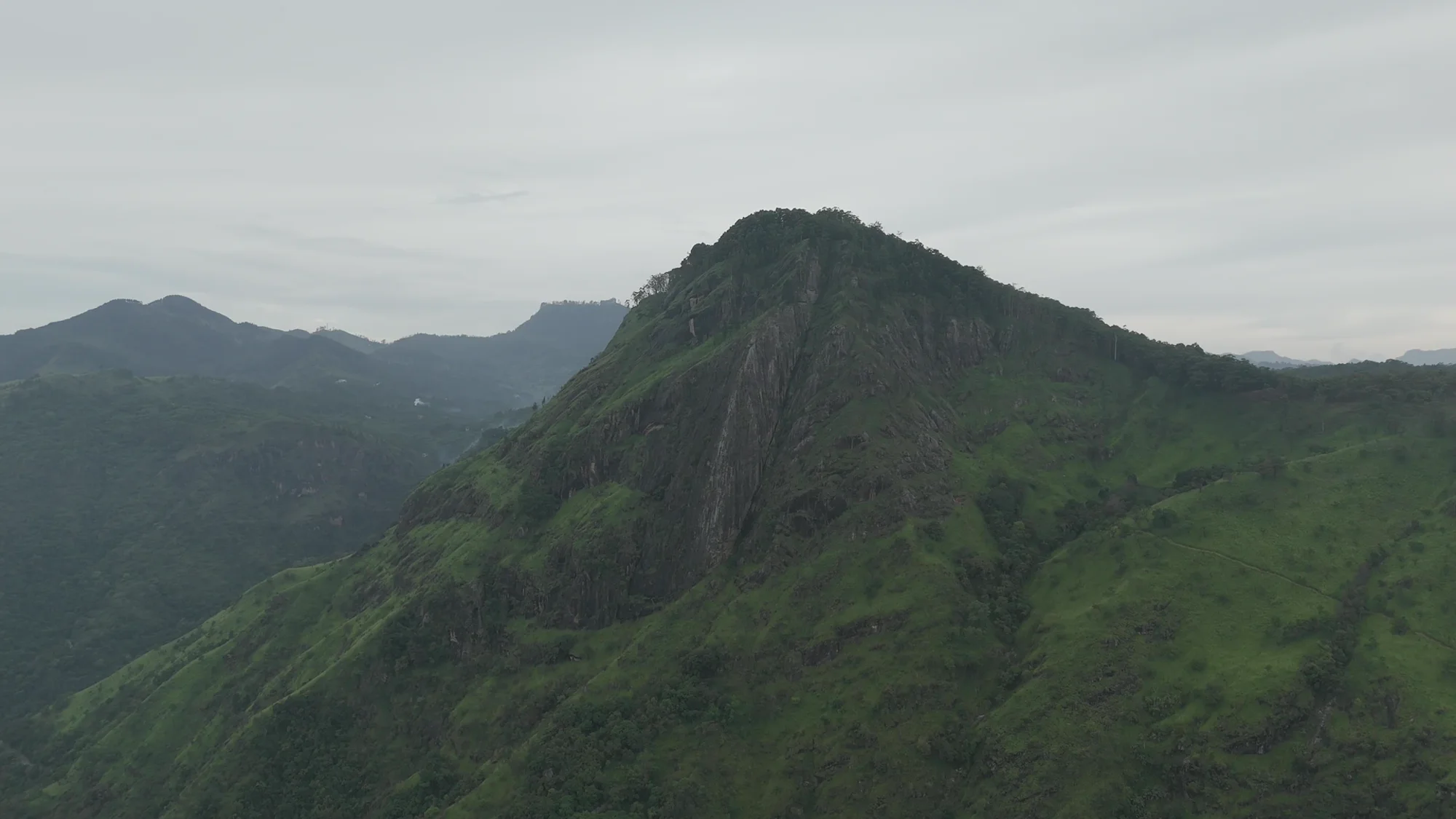 Layers of green Sri Lankan mountain ridges beneath a soft, cloudy sky