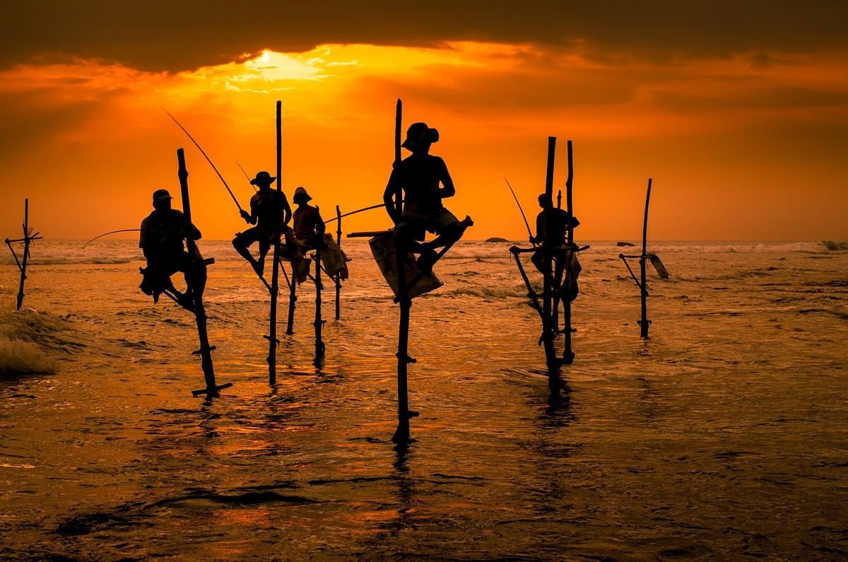 Traditional stilt fishers silhouetted against an orange sunset